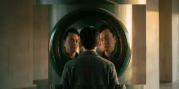 A person observing their distorted reflection in a curved, dark green metallic surface, illustrating cognitive bias in analyzing cultural and technological trends.